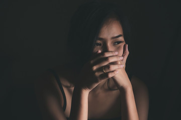 Sad depressed woman suffering from family life. women sitting in dark room and right palm touching her face feeling worry. Young beautiful women thinking how to solve problem.