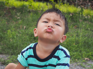Asian Thai cute kid make funny face and mouth while playing outdoors with natural green meadow background in summer. Happy and freedom time.