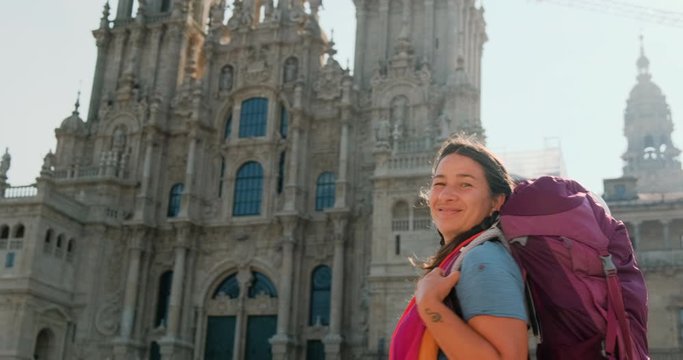 Portrait of happy female pilgrim looking at camera in Santiago de Compostela, Spanish town at the end of Camino de Santiago or Way of St James. Woman smiling in Spain, slow motion