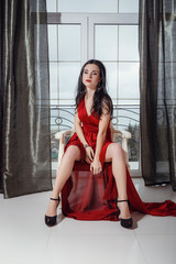 sexy glamour woman with black hair in elegant red dress sitting on armchair