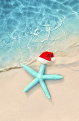 Fototapeta na wymiar Christmas holidays concept. Top view of starfish in santa claus hat on summer sand beach.