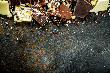 Assorted different types of chocolate. Broken pieces of dark, milk and white chocolate, with nuts, cooking chocolate, shavings. top view copy space