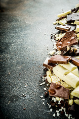 Assorted different types of chocolate. Broken pieces of dark, milk and white chocolate, with nuts, cooking chocolate, shavings. top view copy space