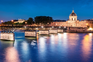 Night cityscape with illuminated academic building Institut de France and pedestrian bridge with lanterns over the river Seine in Paris, France