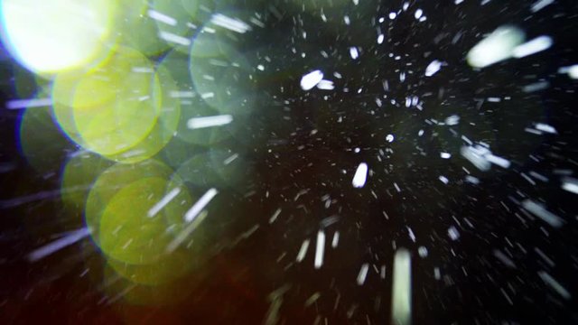 Night winter, heavy snow falls. The big snowflake shines in the strong light. Snowfall sometime faster sometime slower - various amount and intensity