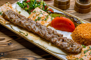 lula kebab from lamb in Turkish on the board with bulgur and vegetables