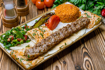 lula kebab from lamb in Turkish on the board with bulgur and vegetables