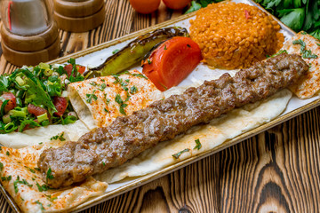 lula kebab from lamb in Turkish on the board with bulgur and vegetables