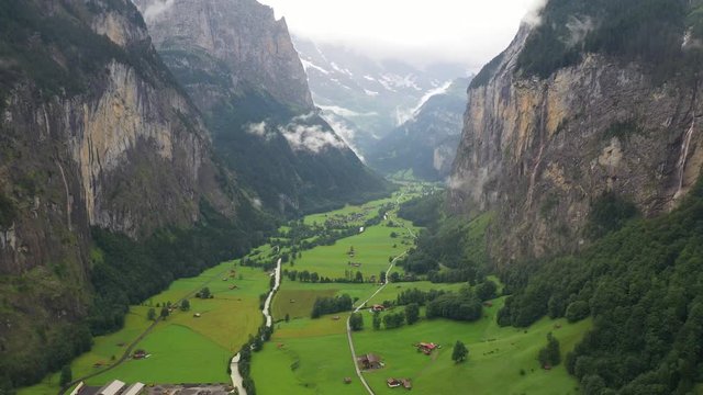Aerial, reverse, drone shot, over the Lauterbrunnen valley, overlooking meadows, buildings and the alpine village, on a foggy, overcast, summer day, in Bernese Oberland, Switzerland