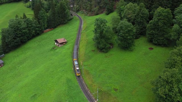 Aerial, descending, drone shot, tilting towards a train on a railway in the alpine mountains, from the Lauterbrunnen village and Wengen town, on a cloudy, summer day, in Bernese Oberland, Switzerland
