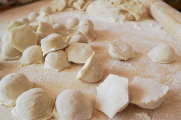 Fototapeta na wymiar Raw dumplings are scattered on a wooden board sprinkled with flour. Cooking a national dish.