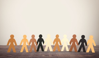 Row of paper people holding hands on table on light background