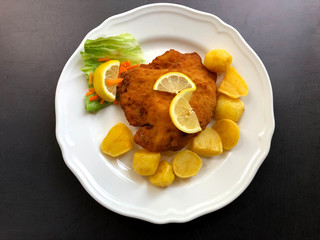 Schnitzel Cordon bleu with fried potatoes and lemon side dish.