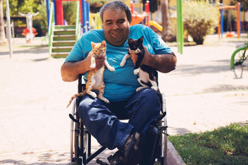 man sit on wheelchair and holding cats on her arms in front of green garden against morning light, hope concept