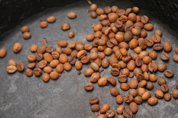 Green coffee beans roasting on the black pan
