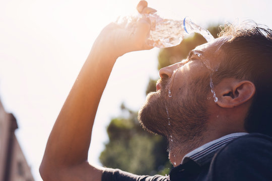 Young man splashing and pouring fresh water from a bottle on his head to refresh against a blue sky background in a summer heat