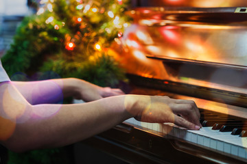 close up of man hand is playing piano with Christmas tree and light.