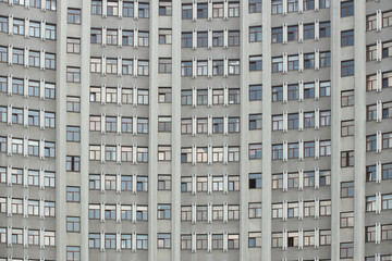 The facade of a tall office building with numerous windows. Architecture of the mid-twentieth century. A monumental building made of reinforced concrete. Wall of an apartment building. Layout design