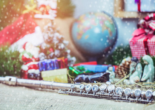 close up of flute with a blurred world globe, Christmas tree, and decoration with gift boxes background, Snow falling in foreground 