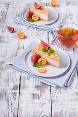 Piece of grated pie with cottage cheese topped with figs and kumquats on ceramic plate on white wooden table