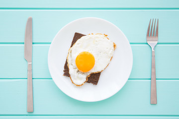 Fried egg and toast for breakfast on wooden table, top view. Colorful turquoise  background, conceptual food. 