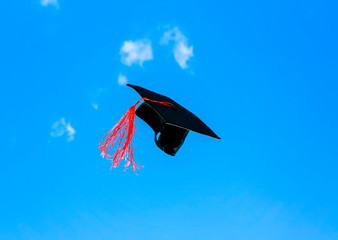 black graduate cap Confederate with a red tassel flying in the blue sky tossed graduate