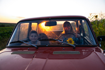 Naklejka premium Happy family on a road trip in their car, young mother driving a red retro car with her teen children, enjoying traveling together