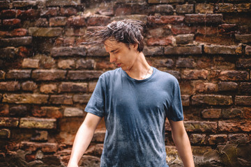 Young man tossing hair standing in the rain against brick wall