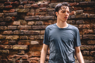 Unhappy displeased teenage boy standing in the rain against brick wall