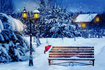 Christmas art card. Santa hat on a bench in the snow against the background of the Christmas winter...
