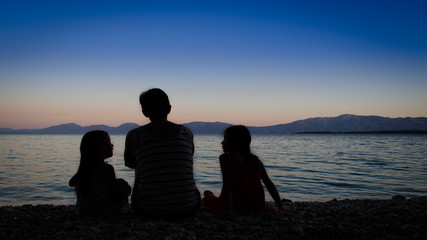 Mother with her two daughters sitting on the beach after sunset