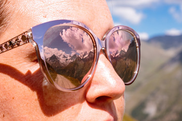 Swiss landscape with snow capped mountains in summer reflecting in sunglasses of a woman. Val d'...