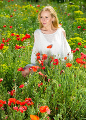 Woman wearing  white dress in poppy field and enjoying summer day