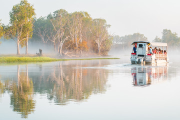 A boat of the Yellow Water Cruise floats in the morning mist on the billabong at sunrise, Kakadu...