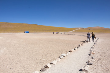 Fototapeta na wymiar Tourists walk towards the bus over sandy pedestrian road in beautiful Atacama desert landscape. Chile - Miniques - Miscanti Lagoons.