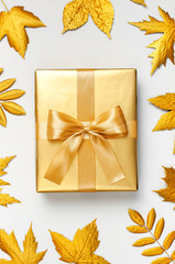 Flat lay Autumn holiday concept. Golden gift or present box with ribbon and golden autumn leaves on light gray background top view copy space. Surprise, congratulation, birthday, greeting card