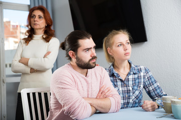 Upset mature woman talking with sad daughter and her boyfriend at home