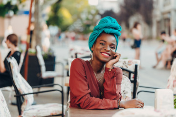 Outdoor portrait of fashionable muslim girl sitting at a table of street cafe