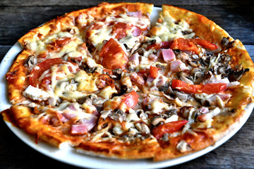 Pizza with cheese, bacon, tomato and herbs in a white bowl on a background of old boards.