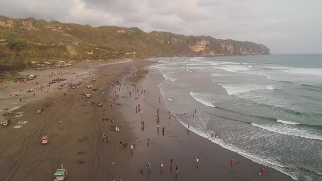 sandy beach parangtritis near ocean with big waves, people in tropical resort at sunset. Yogyakarta, Indonesia. aerial view seascape, ocean and beautiful beach. Travel concept. Indonesia, java