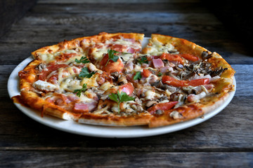 Pizza with cheese, bacon, tomato and herbs in a white bowl on a background of old boards.