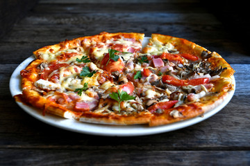 Pizza with cheese, bacon, tomato and herbs in a white bowl on a background of old boards.