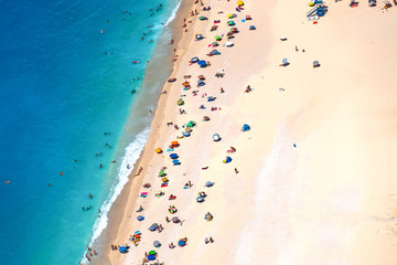  View from above of a white beach with tourists and parasols on a turquoise sea