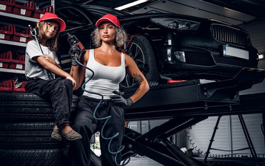 Fototapeta na wymiar Experienced serious woman and her little helper are posing for photographer at dark auto service as great team.