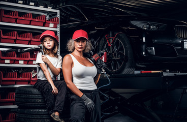Fototapeta na wymiar Experienced serious woman and her little helper are posing for photographer at dark auto service as great team.