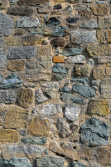 Natursteinmauer aus verschiedenen Natursteinen in verschiedenen Farben von dunkelgrau über einen markanten hervorstechenden roten Ziegelstein bis zum hellen Sandstein