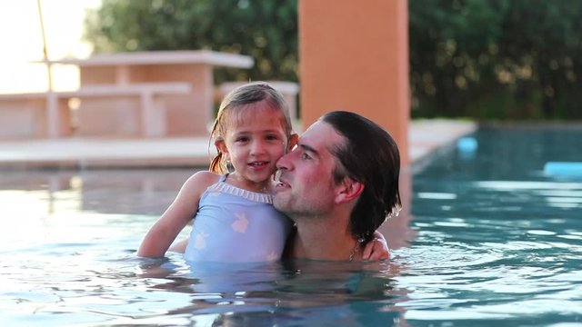 Father and daughter together bonding at the swimming pool dad kissing little girl on the cheek