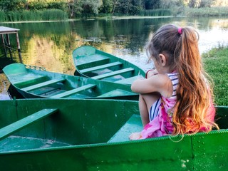Girl sitting in a green boat by the river. The girl sits with her back.