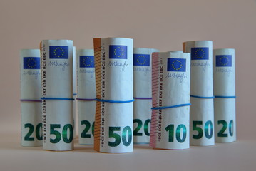 Euro banknotes 50, 20 and 10, rolled in rolls and tied with elastic thin rubbers stands next to each other isolated on creamy color background, close up