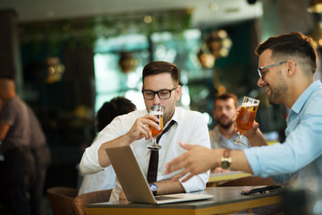 Two young businessmen use a laptop and drink beer